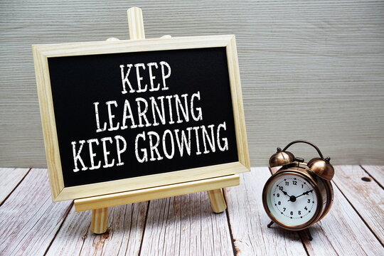 Naklejki Keep Learning Keep Growing text written on chalkboard with alarm clock on wooden background