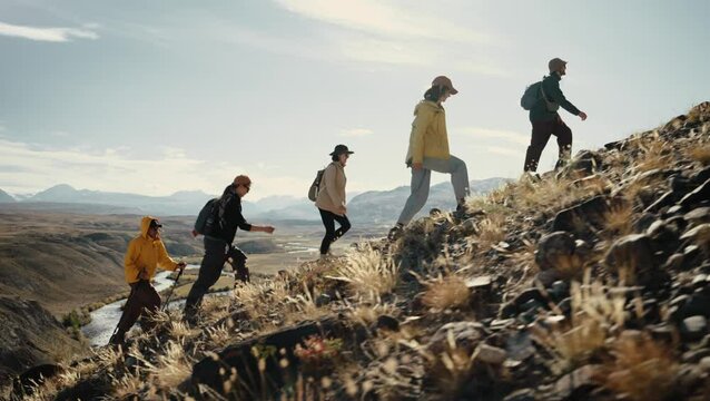 View of a group of five hikers walking up a mountain slope against the backdrop of a mountain valley