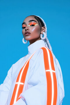 Fashion model wearing futuristic white jacket with orange led stripes and braids on blue background