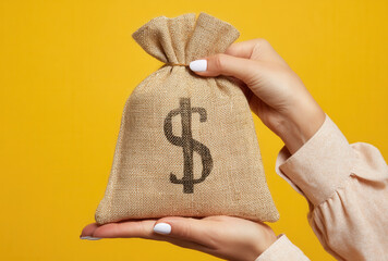 Women's hands elegantly hold a burlap money bag with dollar sign against a vibrant yellow background showcasing financial prosperity