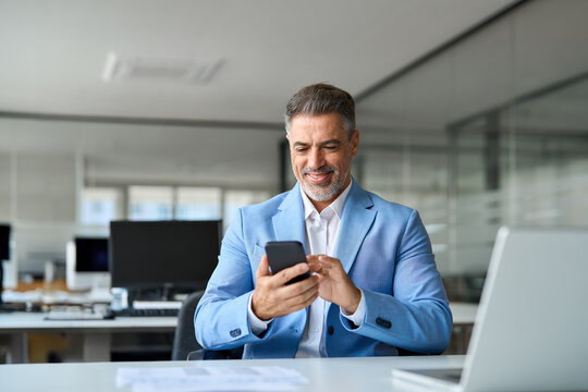 Smiling mature older business man using mobile phone at work. Happy mid aged businessman investor executive looking at smartphone texting in app checking finance banking market on cellphone.
