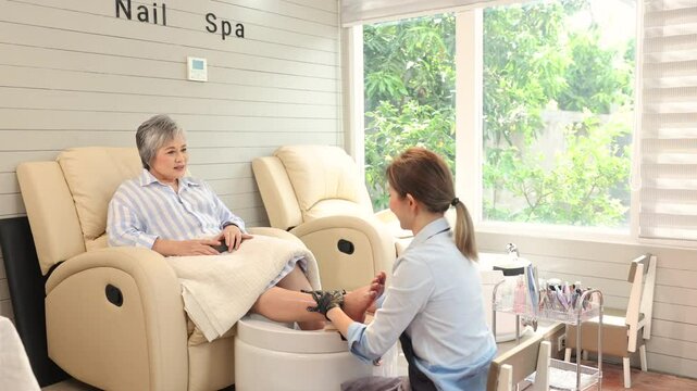 Asian woman enjoying relaxing spa treatment while therapist provides arm massage in cozy modern room, seated in a comfortable chair as part of wellness and personal care experience, modern.
