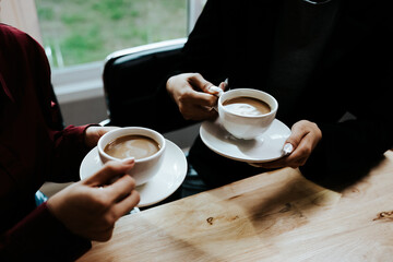 Young adults enjoy coffee and conversation at a cozy café, sharing laughter, bonding, and relaxation in a warm, friendly atmosphere indoors.