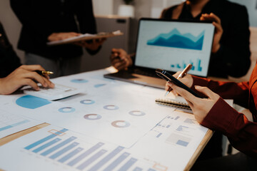 A group of professionals collaborates in an office, analyzing financial graphs and documents to strategize business growth and project success.