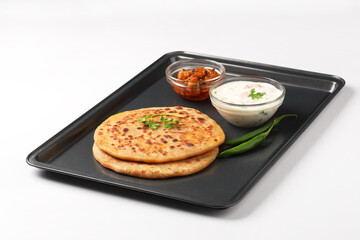 Indian food Aloo Paratha ,Potato stuffed bread served in a black metal tray with raita and mango pickle