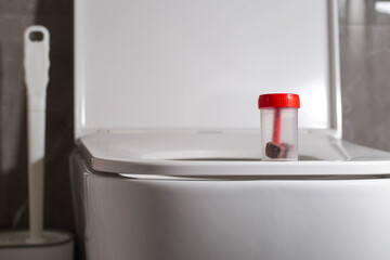 Sterile container with stool test on the toilet bowl in the toilet. Concept of stool testing for calprotectin and occult blood. Copy space for text