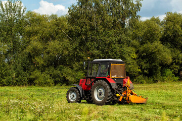 Obraz premium Roadside mowing of grass with a tractor near the road. Mowing roadsides, maintaining roadside areas, copy space for text. Road maintenance organization