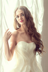 Beautiful and sexy young woman in a white luxurious wedding dress. Preparation for the wedding, romantic morning of the bride. Girl with beautiful long hair