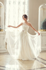 young fragile brunette girl. bride in a luxurious wedding dress in a chic interior with beautiful sunlight from the windows wedding hairstyle and makeup. photo for wedding salt, beauty salon