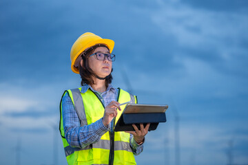 A woman in a yellow safety vest is writing on a clipboard in front of a wind farm. Concept of responsibility and diligence