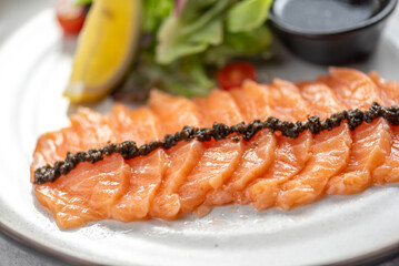 A plate of thinly sliced salmon with a side salad, lemon wedge, and a small dish of dressing.