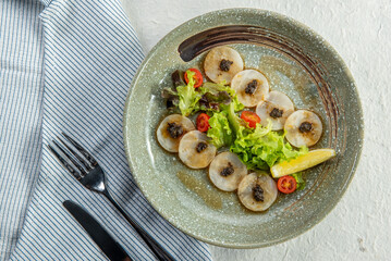 A plate of delicious-looking food with scallops, lemon, and caviar, arranged on a bed of greens, ready to be enjoyed.