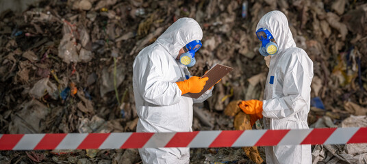 Two scientists in protective suits conducting environmental analysis at waste disposal site with...