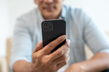 Handsome asian mature old man using smartphone on sofa in living room at home. Happy Portrait of cheerful smiling senior asian man holding cell phone. Mature People and lifestyle