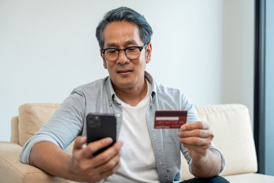 Mature asian old man holding credit card input number in smartphone for payment online. Pay with credit card on cell phone lifestyle technology financial for senior people - Powered by Adobe