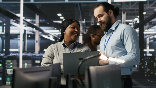 Data center engineering team colleagues collaborating on blade servers maintenance to ensure continuous AI processing. Technicians manage infrastructure supporting machine learning pipelines, camera A