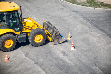 Modern yellow forklift stands on the road near the dug up road. Concept of emergency service for elimination of accident in water supply and sewerage. Copy space for text