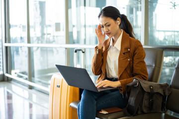 Stressed young asian businesswoman working laptop online at the airport terminal while waiting for...
