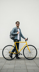 Obraz premium Stylish Cyclist: Man with Yellow Bike, Backpack & Sunglasses Posing on Pavement. Urban Lifestyle & Transportation!