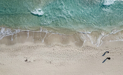 People walking on tropical beach with turquoise water and white sand. Drone aerial view of exotic coast