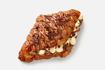 Delicious croissant filled with cream and topped with chocolate shavings on white background