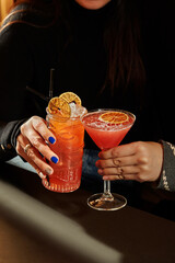 Woman holding tropical tiki cocktail and cosmopolitan cocktail with orange garnish