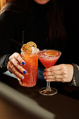 Woman holding two fancy cocktails with orange garnish in a tiki mug and martini glass