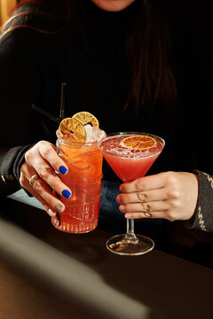 Woman holding two fancy cocktails with orange garnish in a tiki mug and martini glass