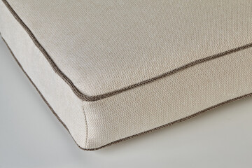 Close-up of beige fabric cushion with brown piping detailing, showcasing high-quality upholstery