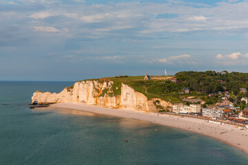 Beautiful coastline in Etretat, France with charming houses along the shore. Boats float gently in the water beneath scenic cliffs on a sunny day.