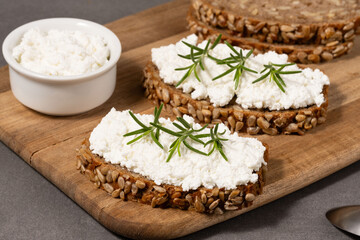 Delicious rye bread topped with creamy cheese and fresh herbs on a rustic wooden board