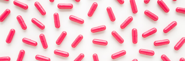 Red capsule pills for improve of iron level in blood on white table background. Wide banner. Medicine pattern. Closeup. Top down view.