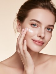 Close-up of young woman with healthy radiant skin and skincare cream, beige background.