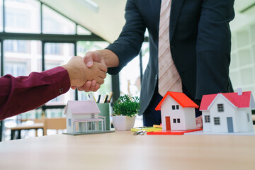 .Cheerful Asian real estate professional shaking hands with happy new homeowner, closing sale while holding documents and smiling. Couple shaking hands thanking real estate agent for successful apartm