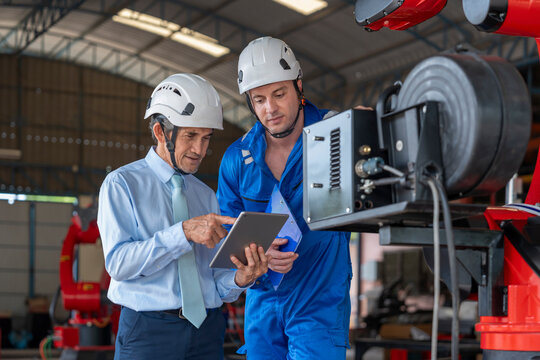 factory workers in maintenance robot machine,senior man expert manager using tablet computer giving advice young male caucasian technician in small industry