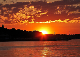 Naklejka premium Golden coastal sunset view with silhouetted shoreline and vibrant skies