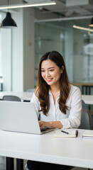 Asian Woman Working on Laptop: Happy Student, Office Professional, or Entrepreneur at Desk with Notebook & Pen. Modern Workspace Vibe!