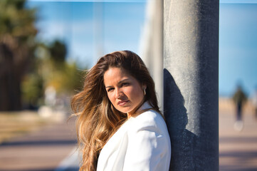 Obraz premium Portrait of a young and beautiful blonde woman leaning on a lamppost and looking at the camera, the woman is serious and wearing a white jacket.