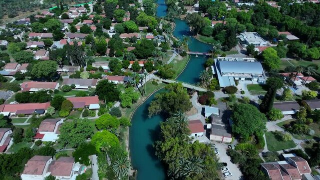 Aerial Beautiful Shot Of Houses In Kibbutz, Drone Flying Forward Over River Stream On Sunny Day - Nir David, Israel
