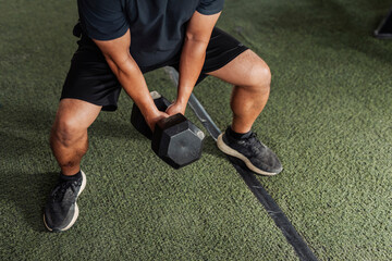 A fit anonymous man performs a dumbbell plie squat with wide stance to target inner thighs and lower body at open gym.