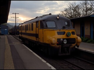 Naklejka premium a train at a train station. The train is a yellow and black train with multiple windows and doors.