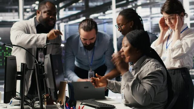 Engineering team in data center panicking after receiving critical error popup on PC monitor. Server room coworkers alerted by bugs causing low gear performance while troubleshooting systems, camera A
