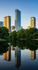 Fototapeta premium Cityscape Reflection: Serene Lake Views of Modern Buildings, Lush Greenery, & Urban Tranquility at Golden Hour