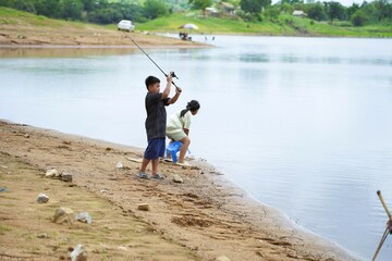 Brother and sister enjoy summer fishing with fishing rods by the water.