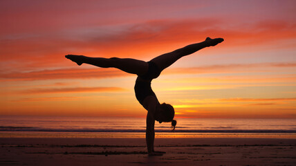 Gymnast in handstand silhouette against a fiery sunset