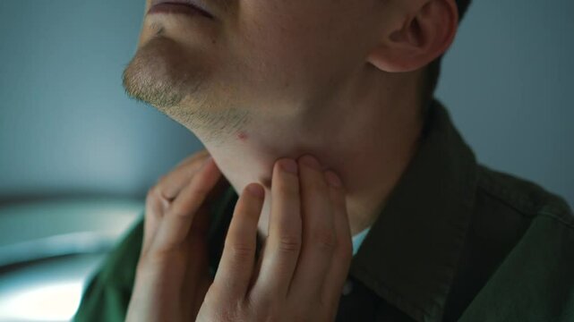 A guy with European appearance touches his sore throat.
The man has a cold and is suffering from a sore throat.
It hurts for a person to swallow.
Redness in the throat.
Infection, sore throat, pain