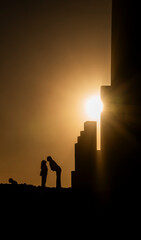 Fototapeta premium A couple is kissing in front of a building. The sun is setting and the sky is orange