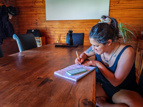 Woman Writing in Notebook at Wooden Table in Cozy Room of Australia