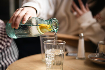 Pouring water into glass with lemon in a cozy cafe setting