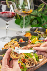 Spreading soft cheese on toasted bread with gourmet appetizers and wine in the background